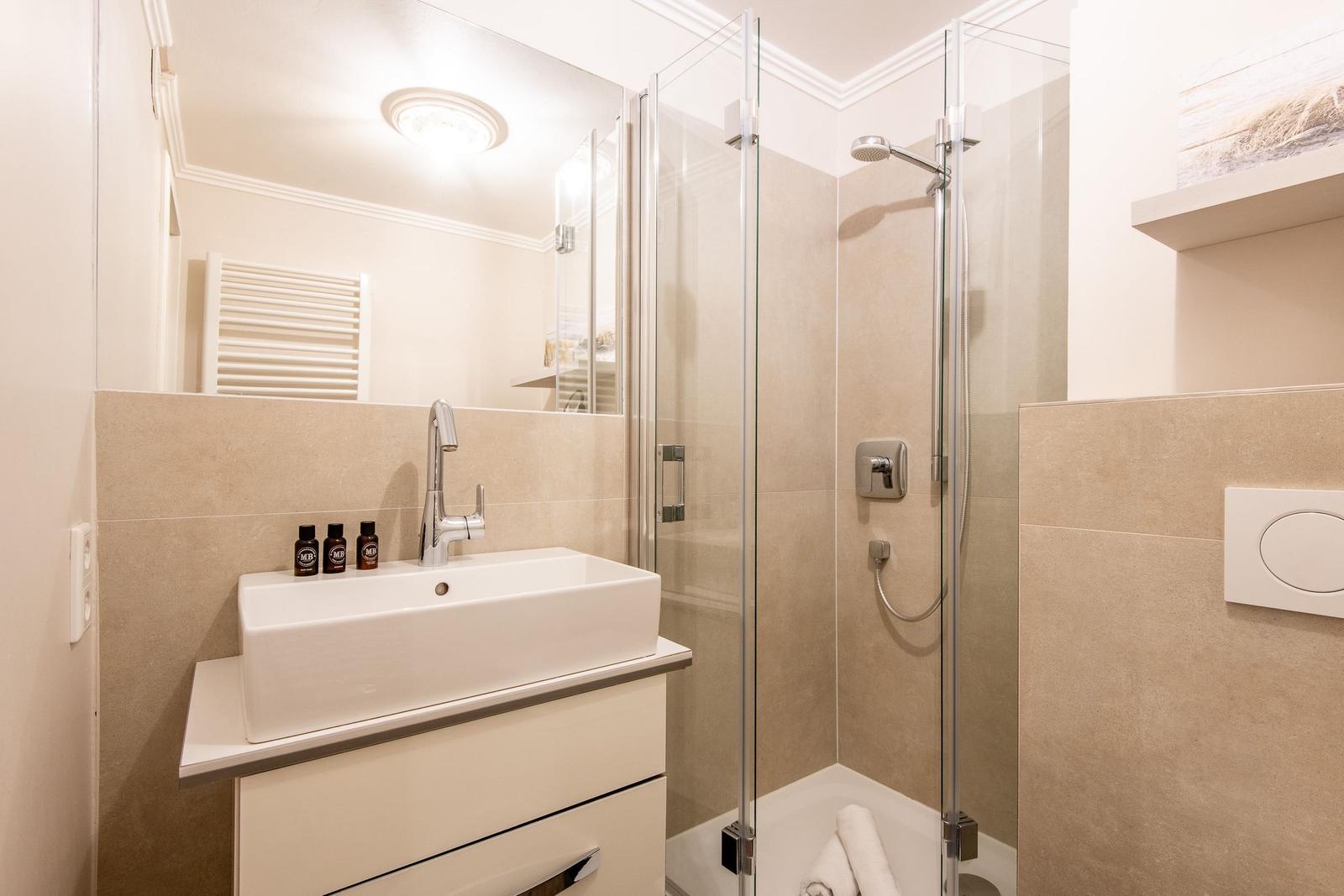 Badezimmer mit Dusche, Waschbecken und Spiegel.