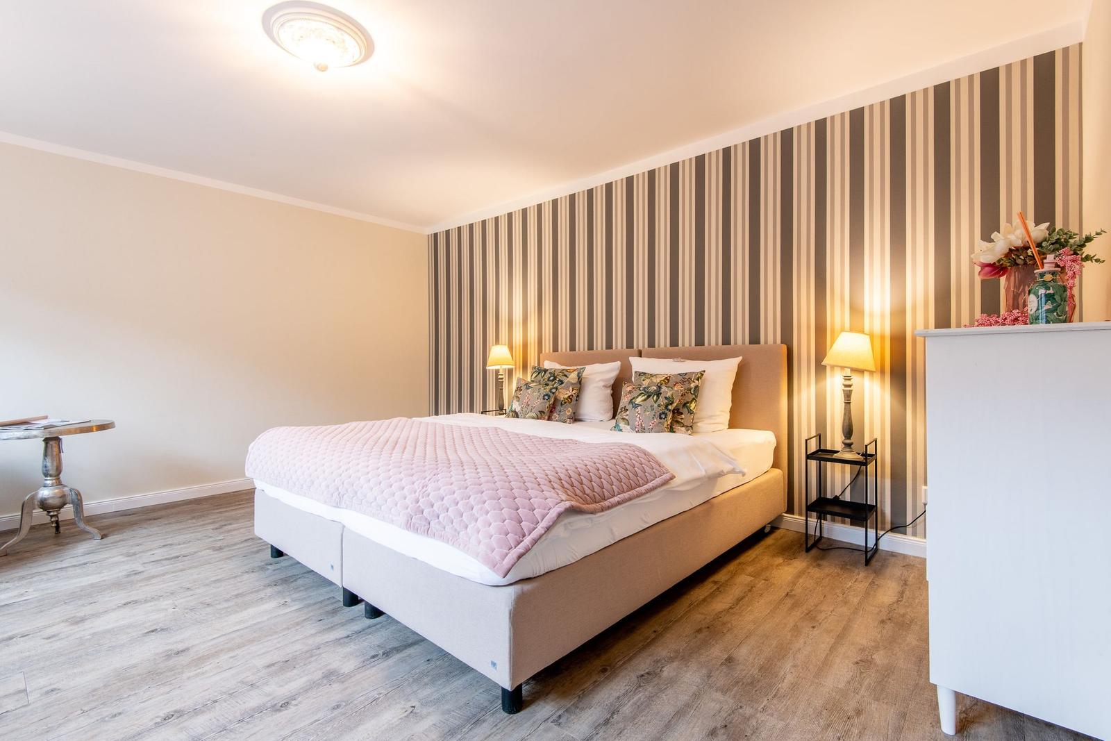 Schlafzimmer mit Bett, Streifenwand und Nachttischen.