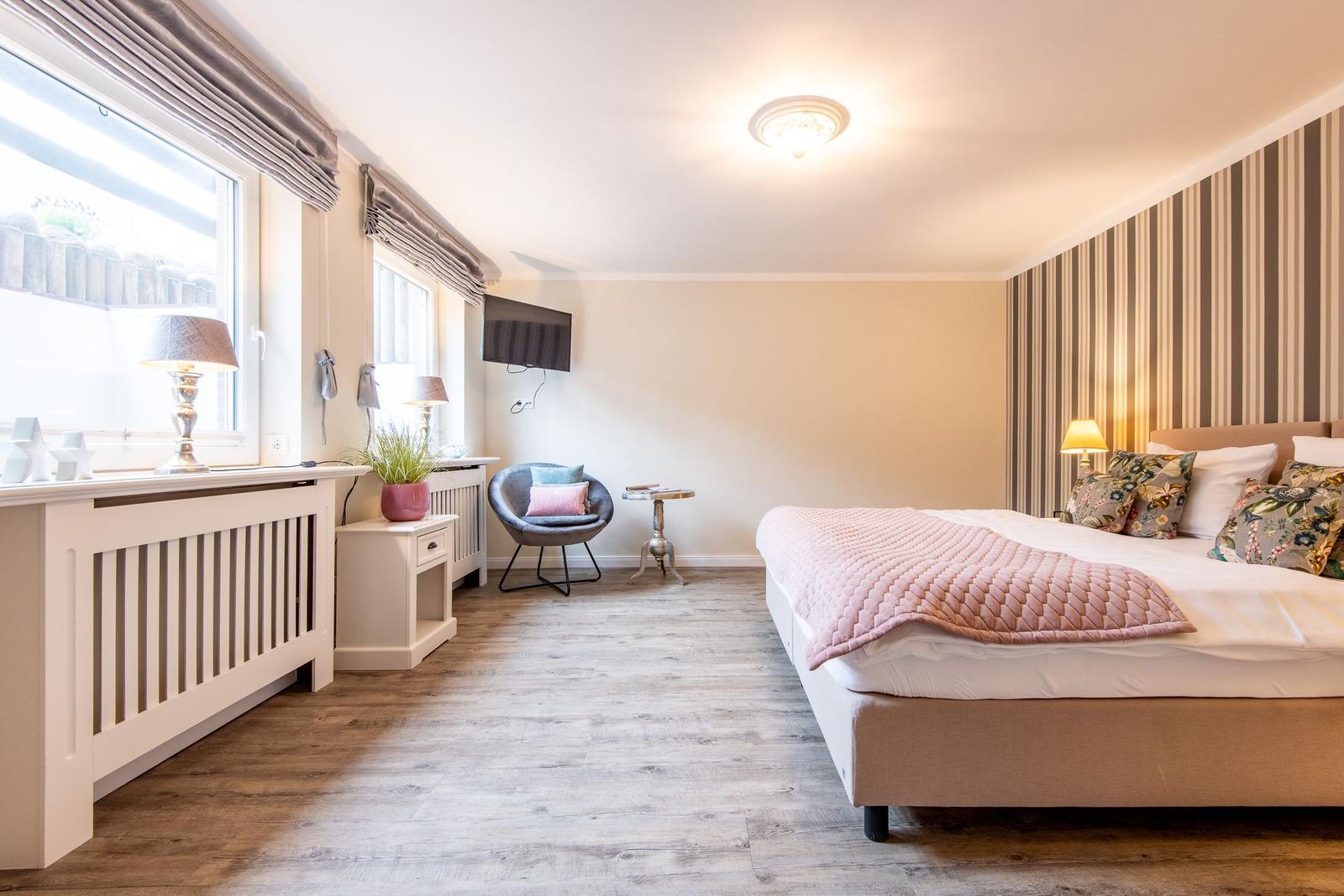 Schlafzimmer mit Bett, Fenstern, Stuhl und Wandbehang.