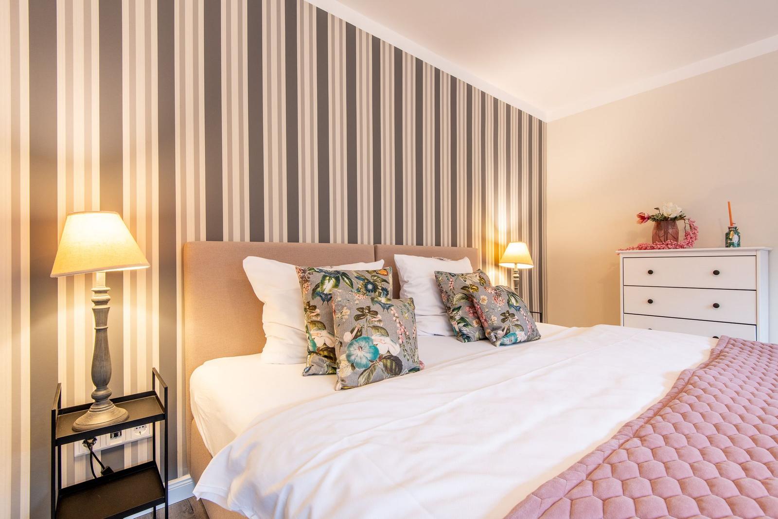 Schlafzimmer mit Bett, Kissen, Nachttisch und Schrank. Wand mit Streifen tapete.