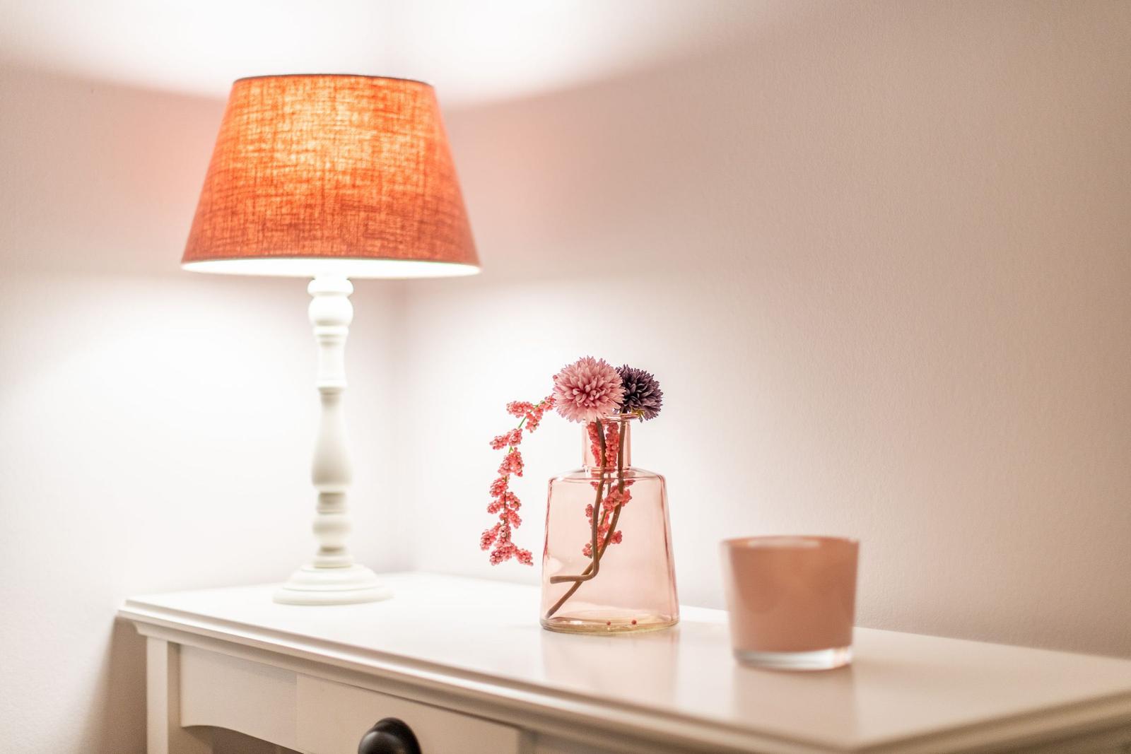 Weißer Nachttisch mit Lampe, Vasen und Kerze.