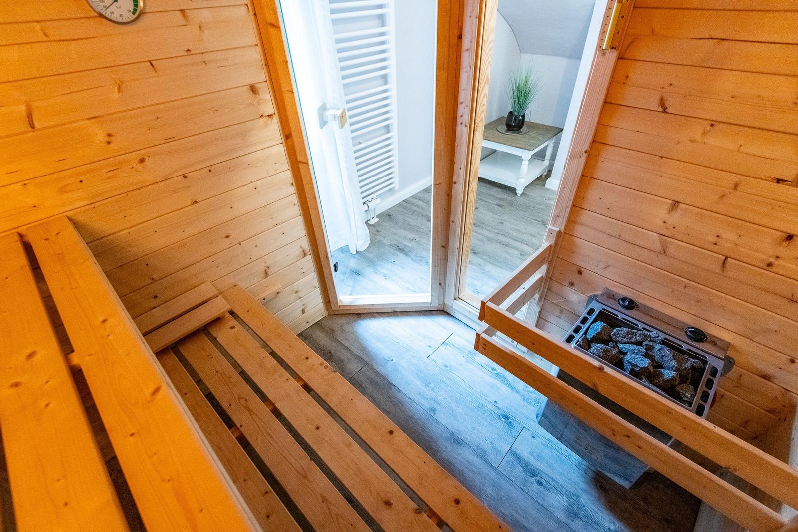 Sauna mit Holzbank und Steinofen. Durchgang zu einem Raum mit Heizkörper.