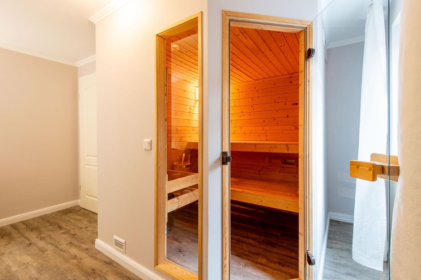 Sauna mit Holzbank und warmem Licht. Tür offen, Blick ins Innere.