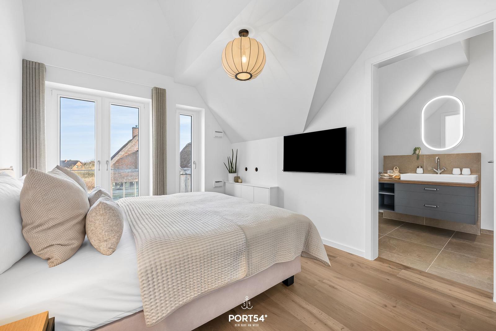 Bedroom with sloped ceiling, bed, TV, and access to bathroom.