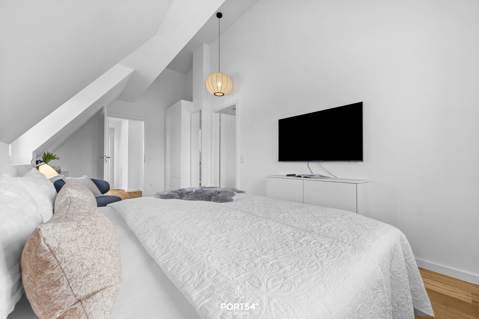 Bedroom with sloped ceiling, bed, TV, and pendant lamp.