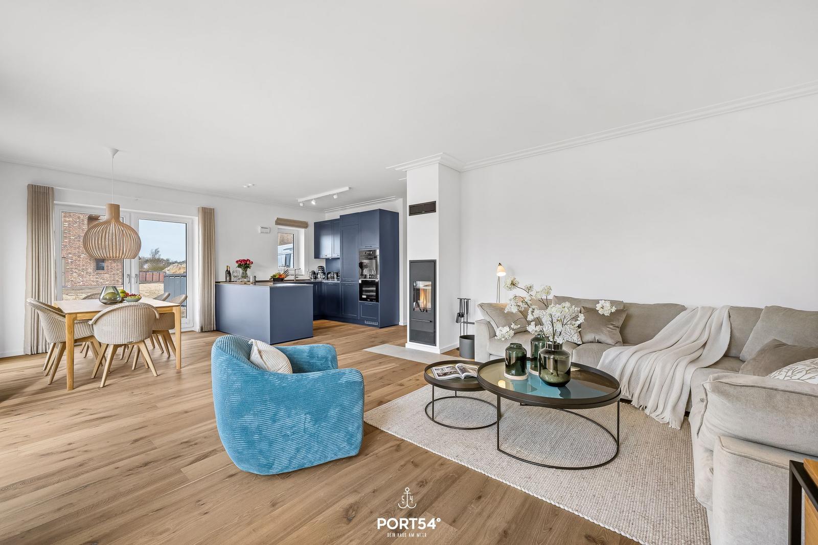 Living area with sofa, coffee table, and blue seating. Kitchen with blue cabinets and dining table.