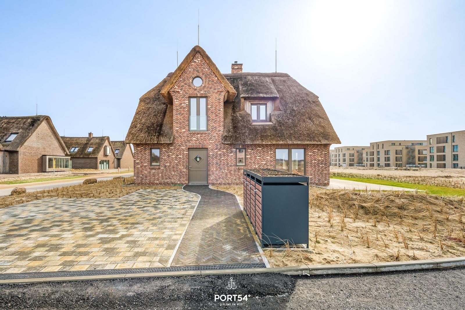 House with thatched roof and brick facade, paved courtyard and modern windows.