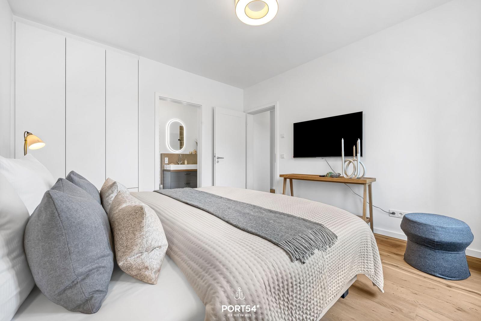 Bedroom with bed, TV, and bathroom in the background.