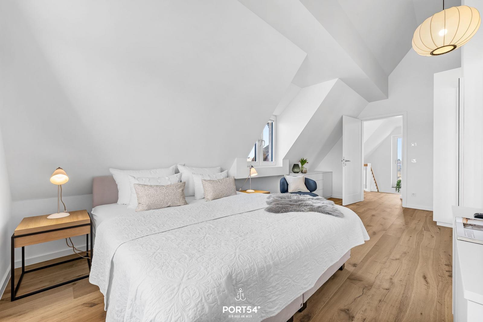 Bedroom with sloped ceiling, bed, nightstand, and lamp.