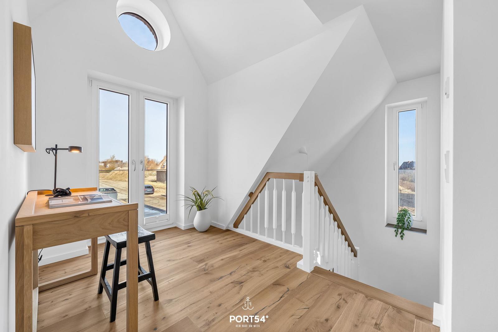 Helle Wohnung mit Holzboden, Schreibtisch, Treppe und Fenstern.