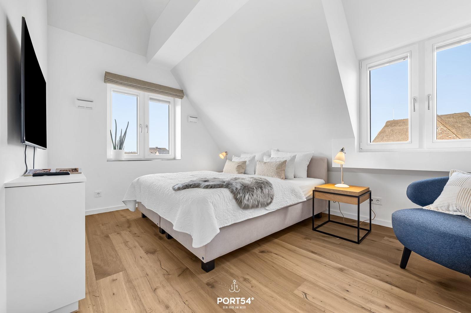 Schlafzimmer mit Dachschrägen, Bett, TV und Sessel.