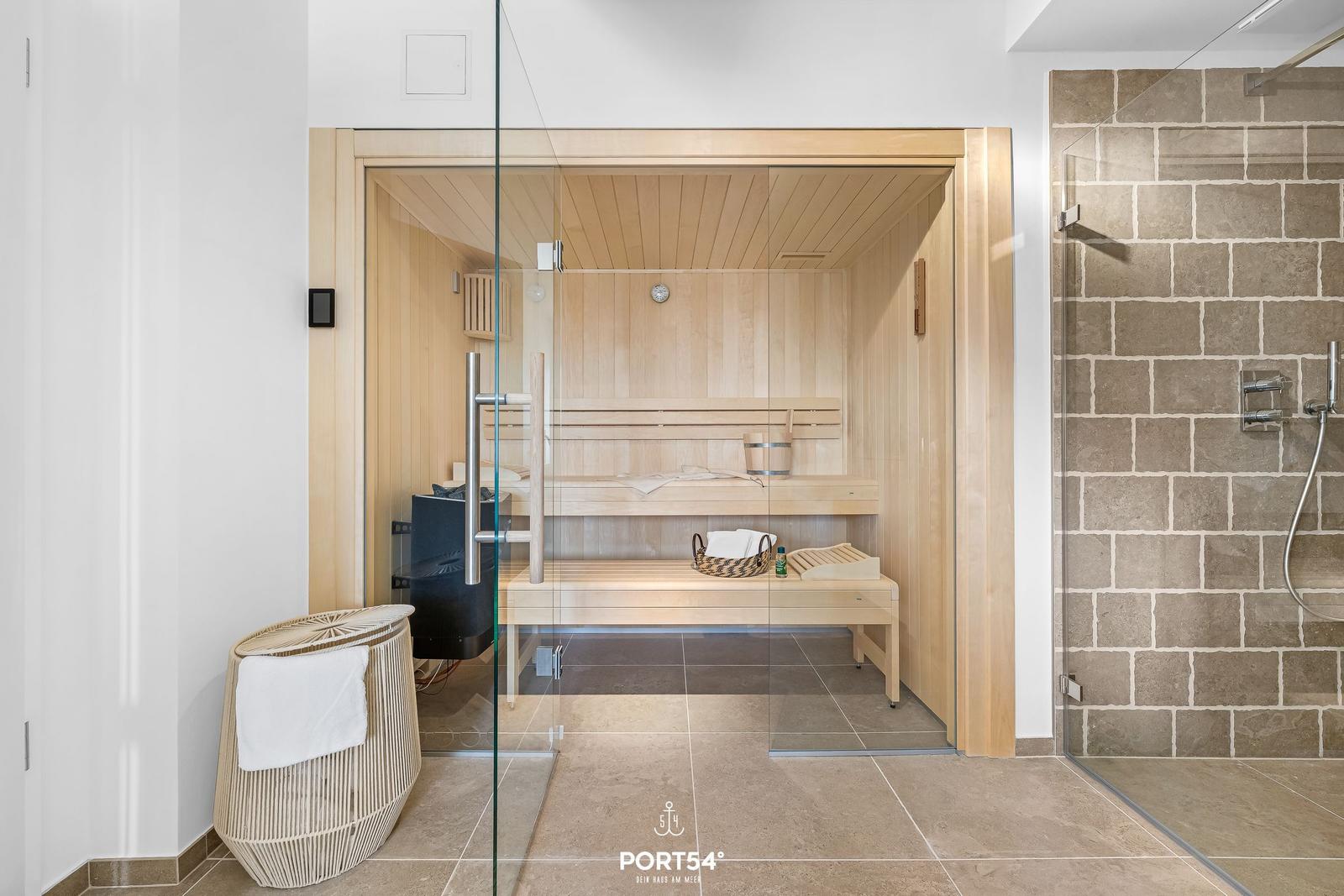 Sauna mit Holzbank und Glaswand. Nebenher Duschbereich mit Steinwand.