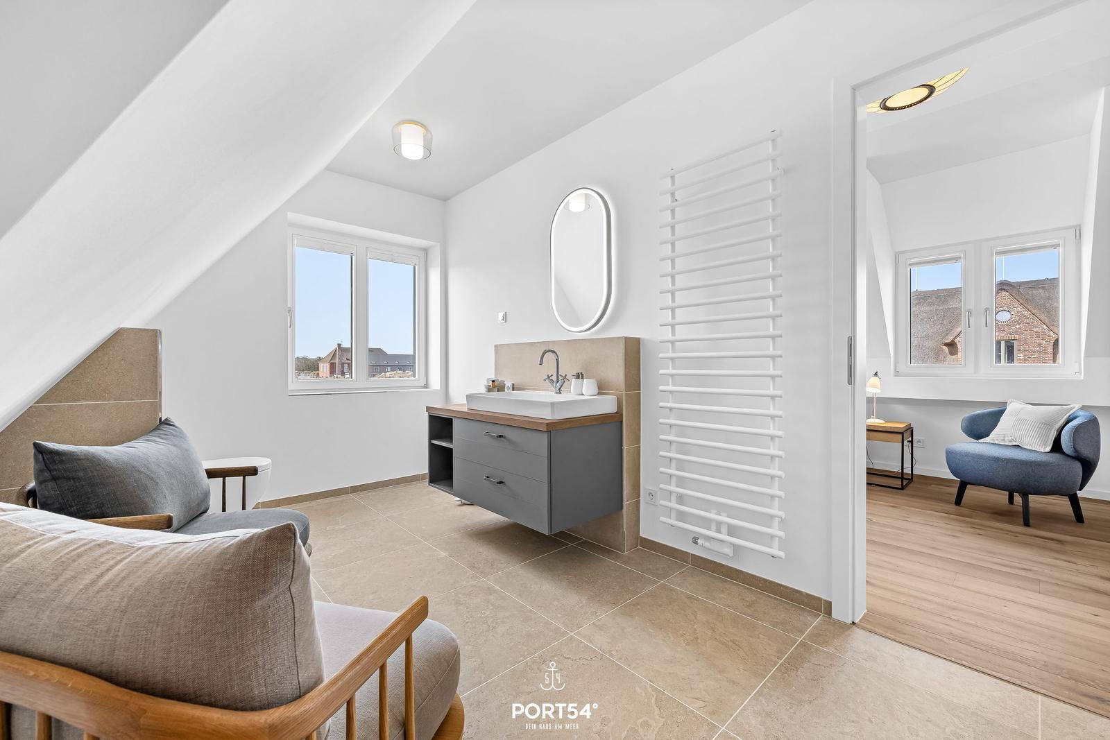 Schlafzimmer mit Dachschrägen, Bad und Sitzgelegenheit. Fenster mit Blick auf Außenbereich.
