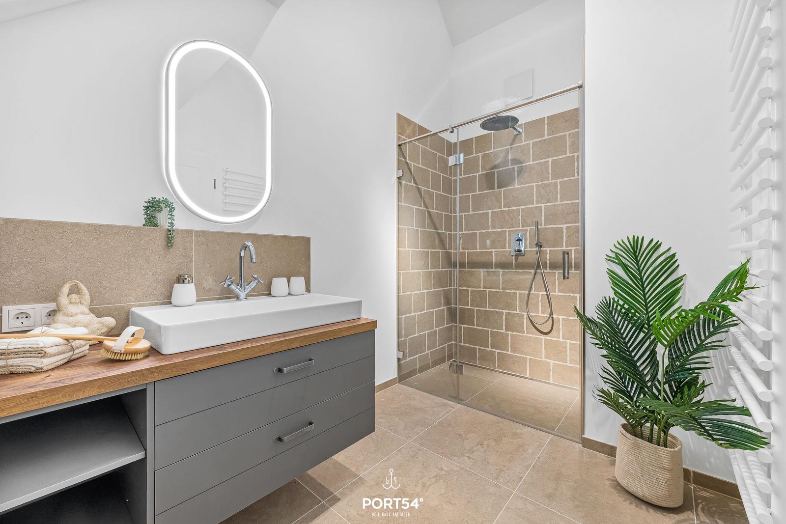 Badezimmer mit Dusche, Waschbecken und Pflanze.