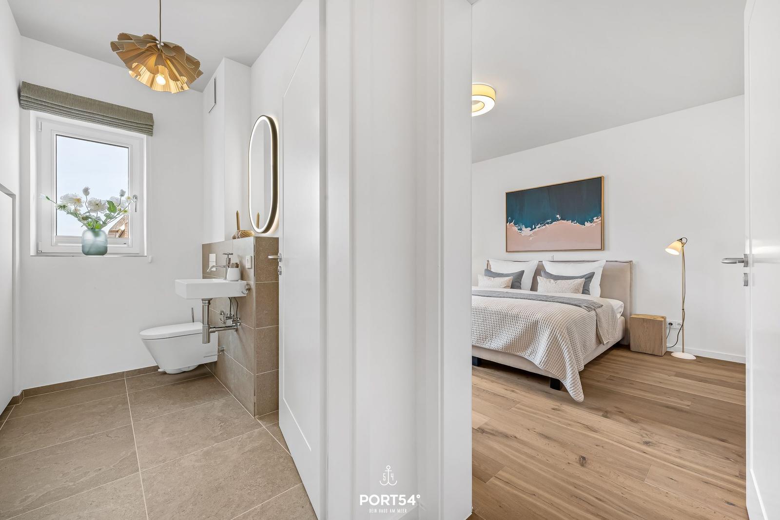 Badezimmer mit Waschbecken und Toilette. Nebenraum mit Bett und Wandbild.