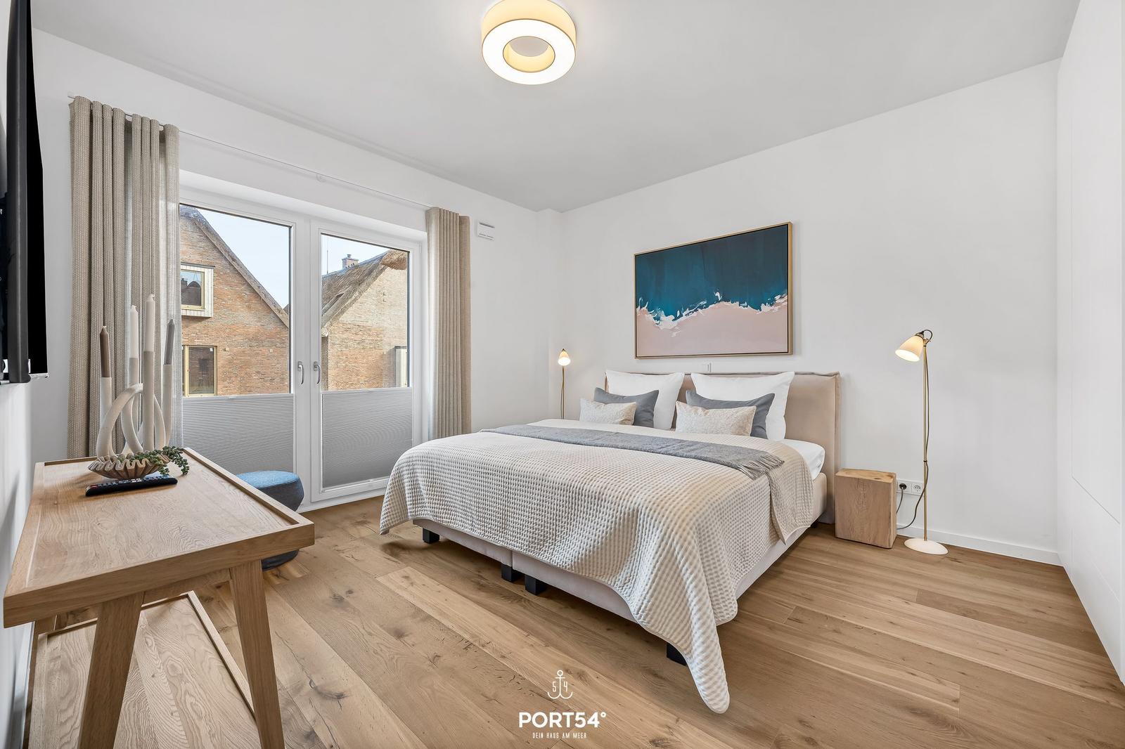 Schlafzimmer mit Bett, Schreibtisch und Fenster zur Terrasse.