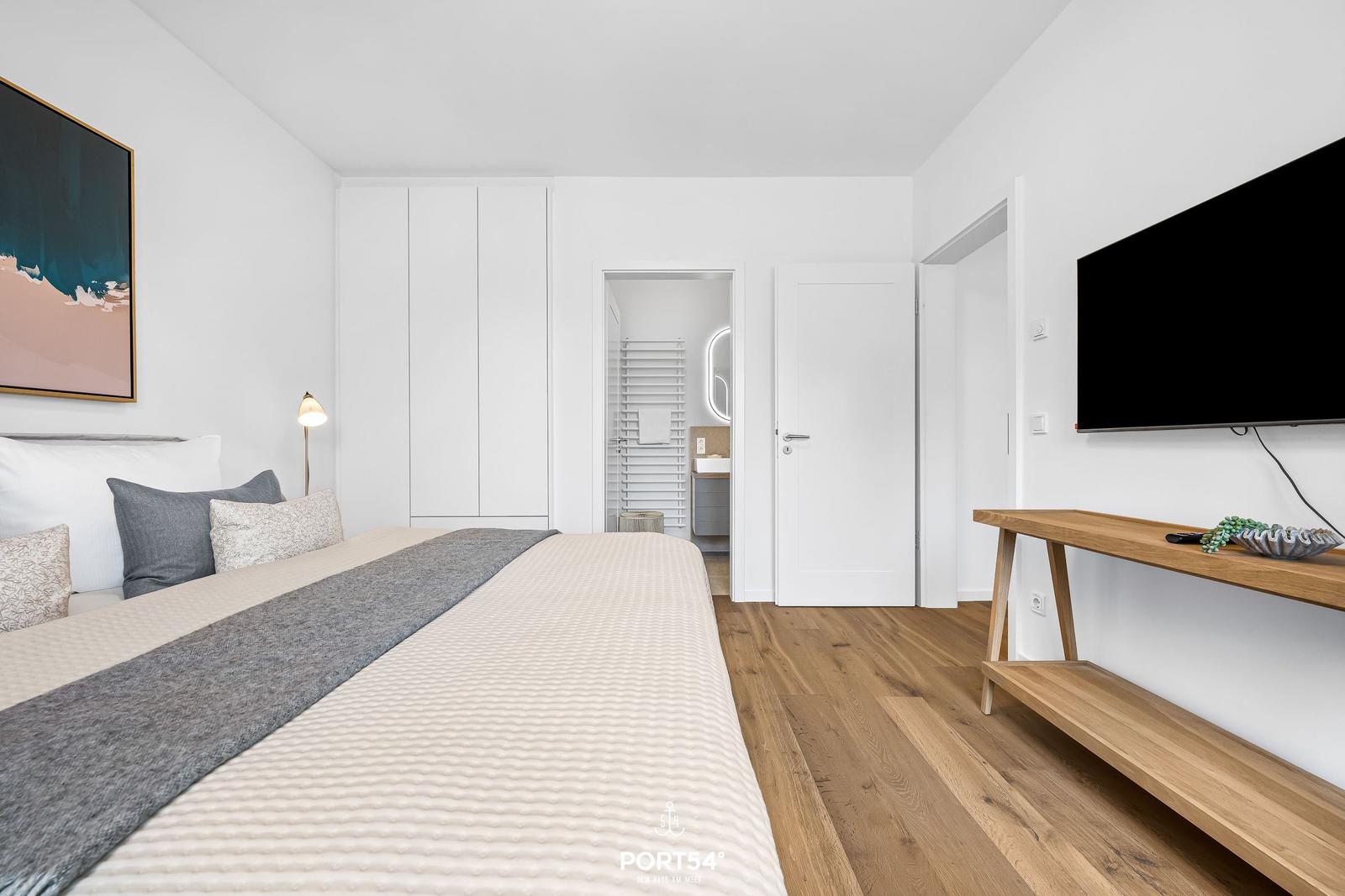 Schlafzimmer mit Bett, TV und Holzboden. Anschlussraum mit Bad und Dusche.