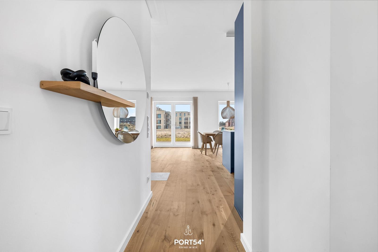 Haus mit Holzboden und runden Spiegel. Durchgang zur Essnische mit Tischen und Stühlen.