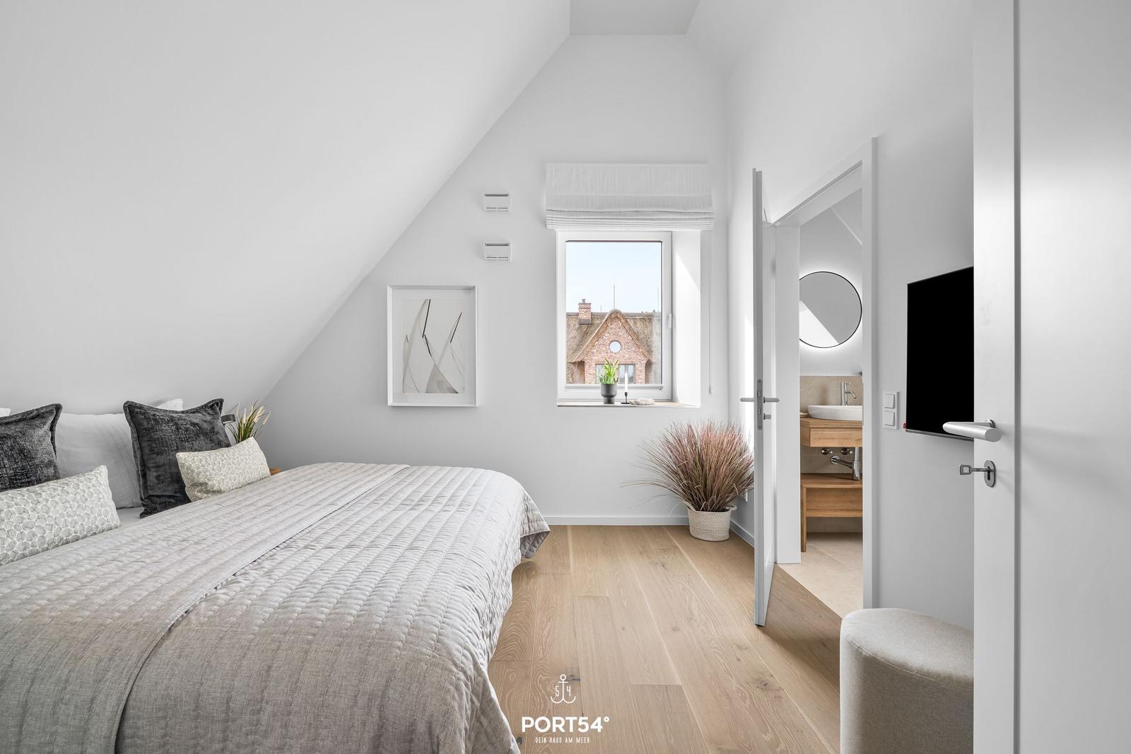 Bedroom with sloped ceiling, window, and adjacent bathroom.