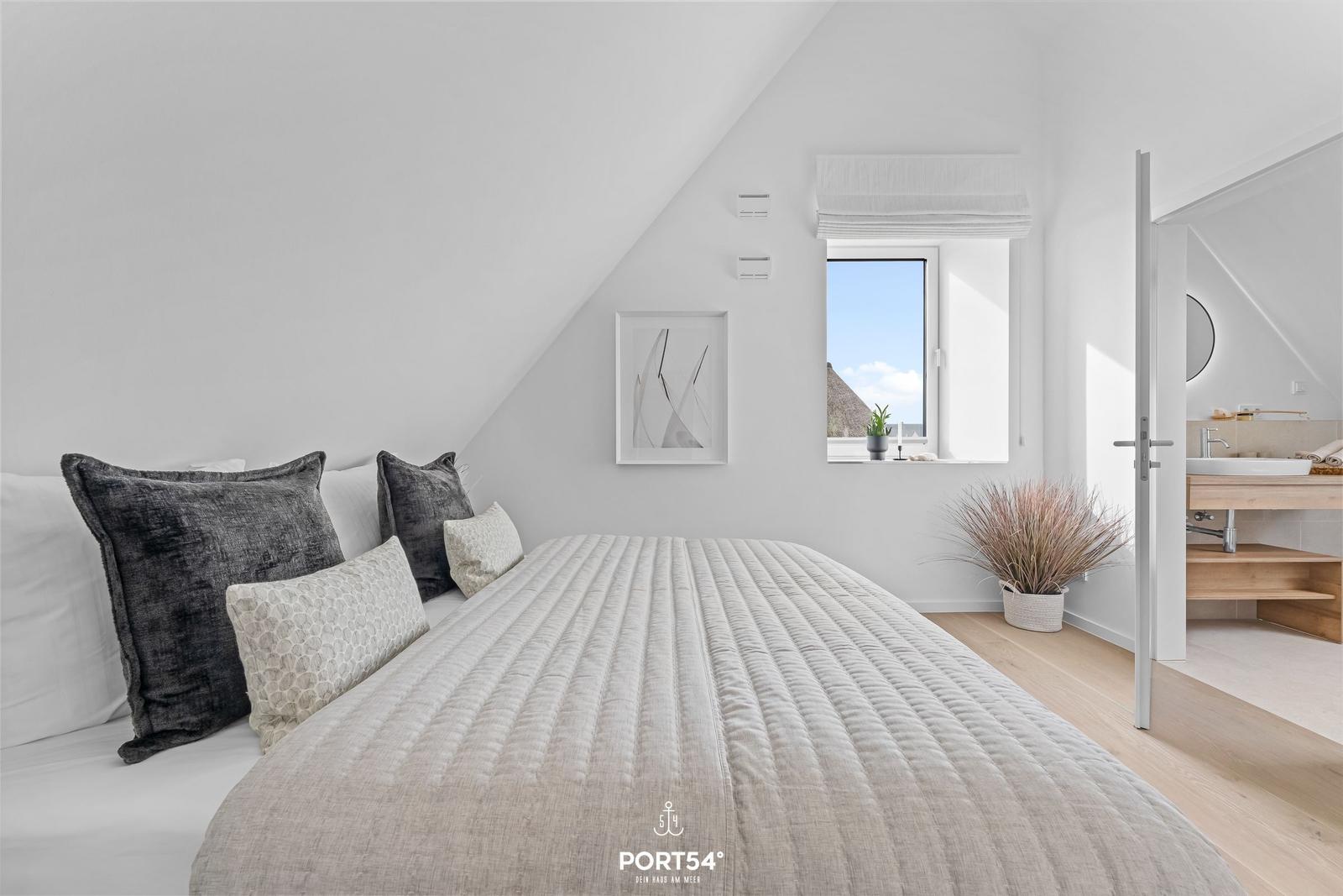 Bedroom with sloped ceiling, bed, window, and adjacent bathroom.