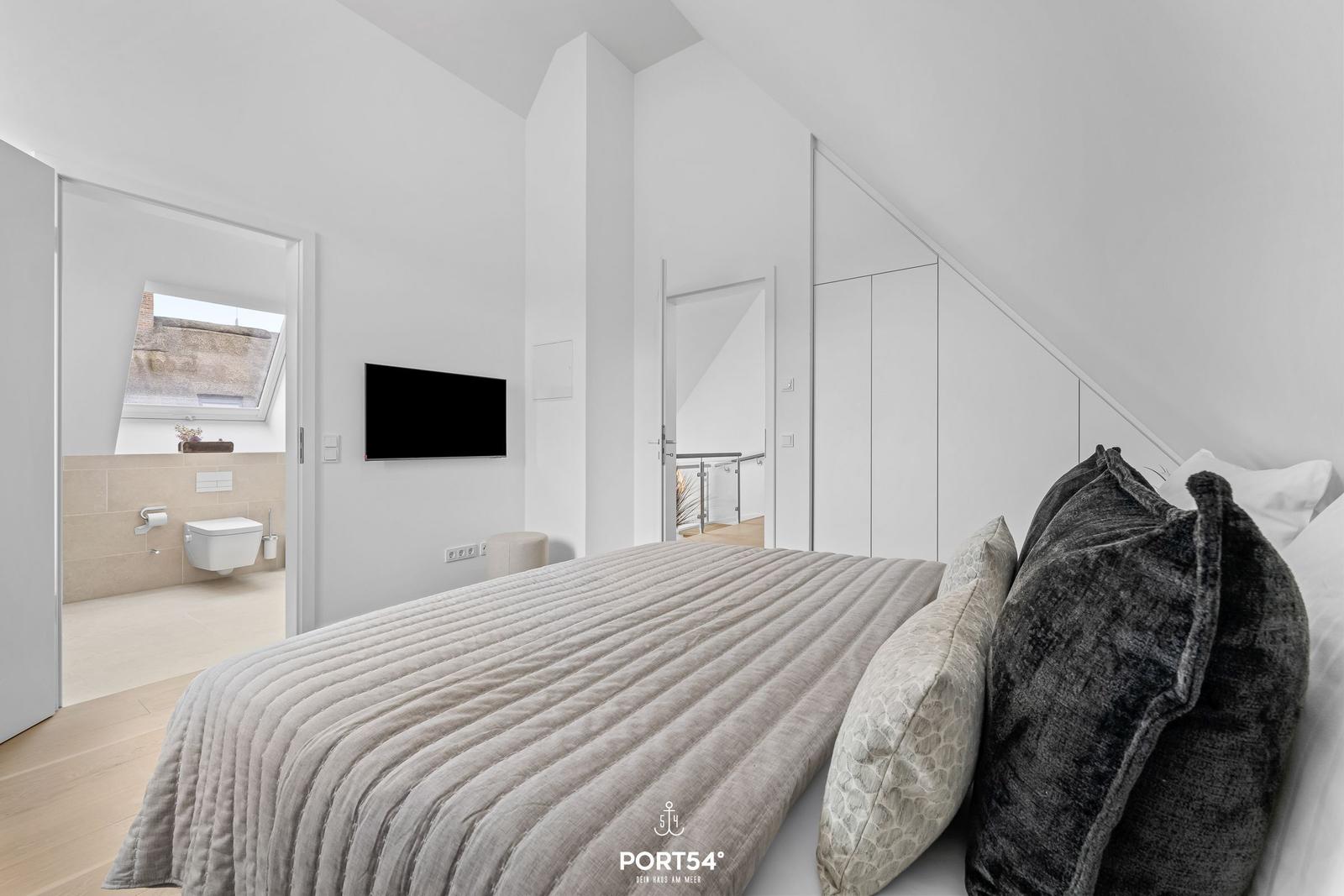 Bedroom with double bed, TV, and view into the modern bathroom.