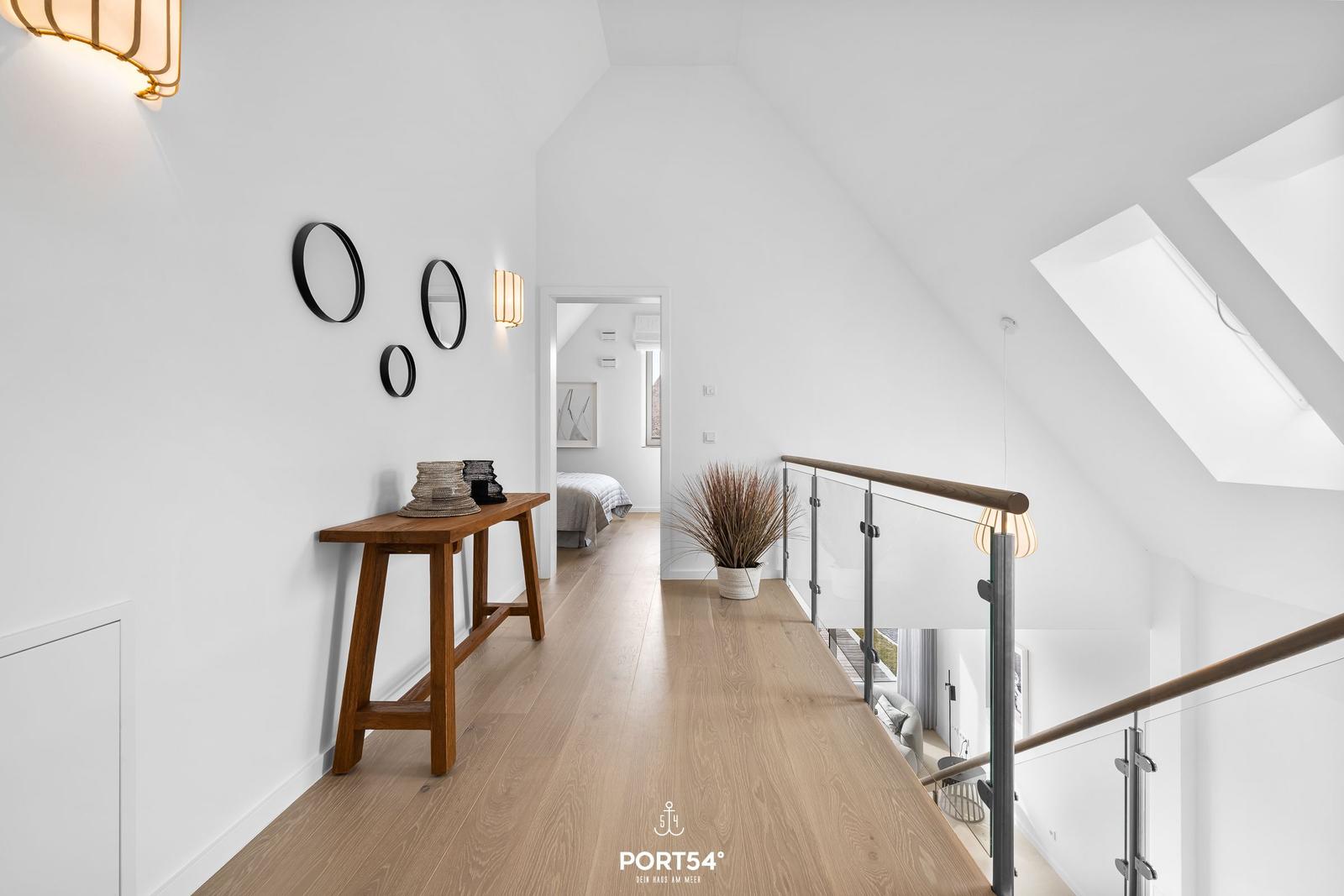 Bright gallery with wooden floor, wall decor, and view into bedroom.