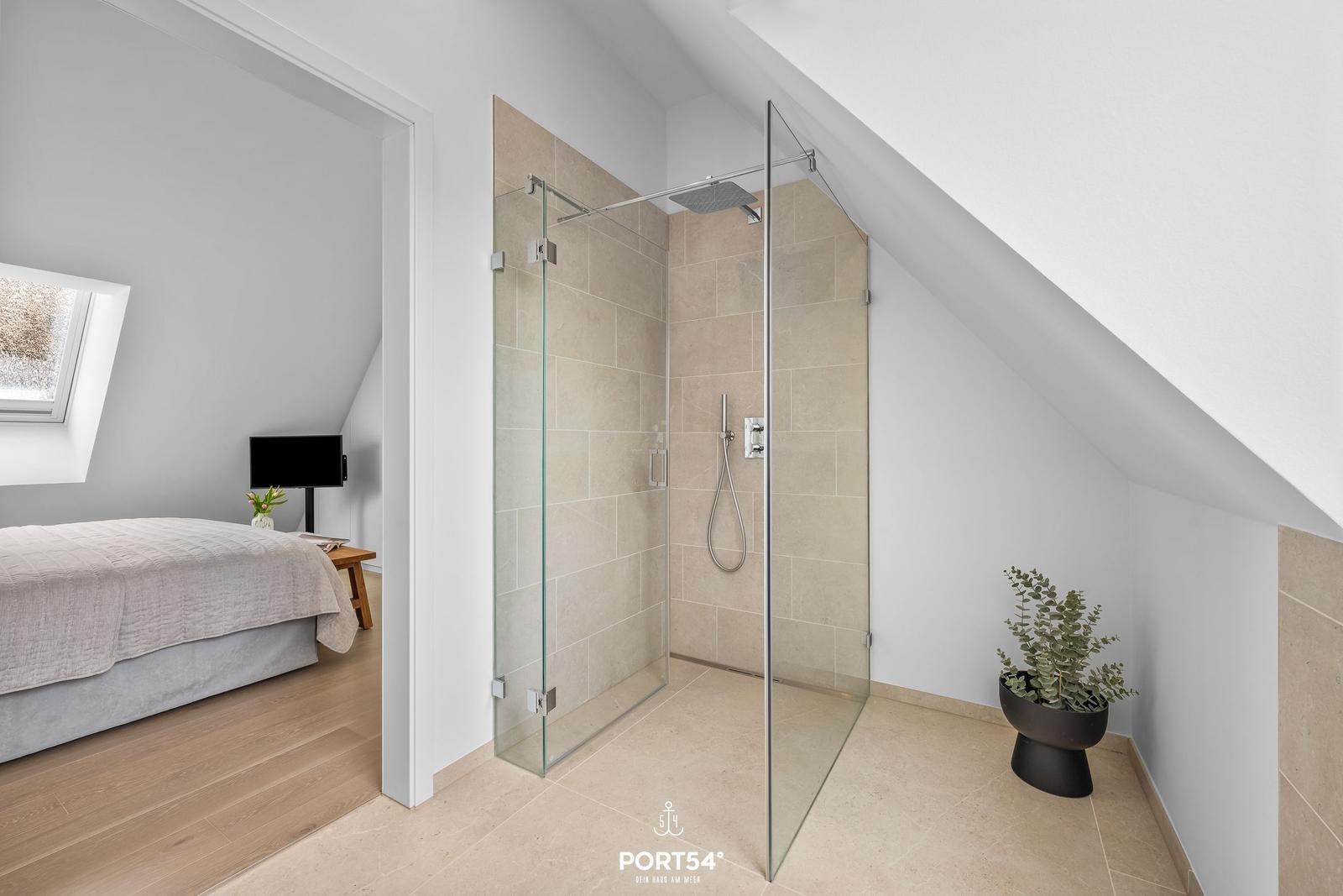 Duschkabine mit Glaswand, beige Fliesen und Pflanze im Schlafzimmer