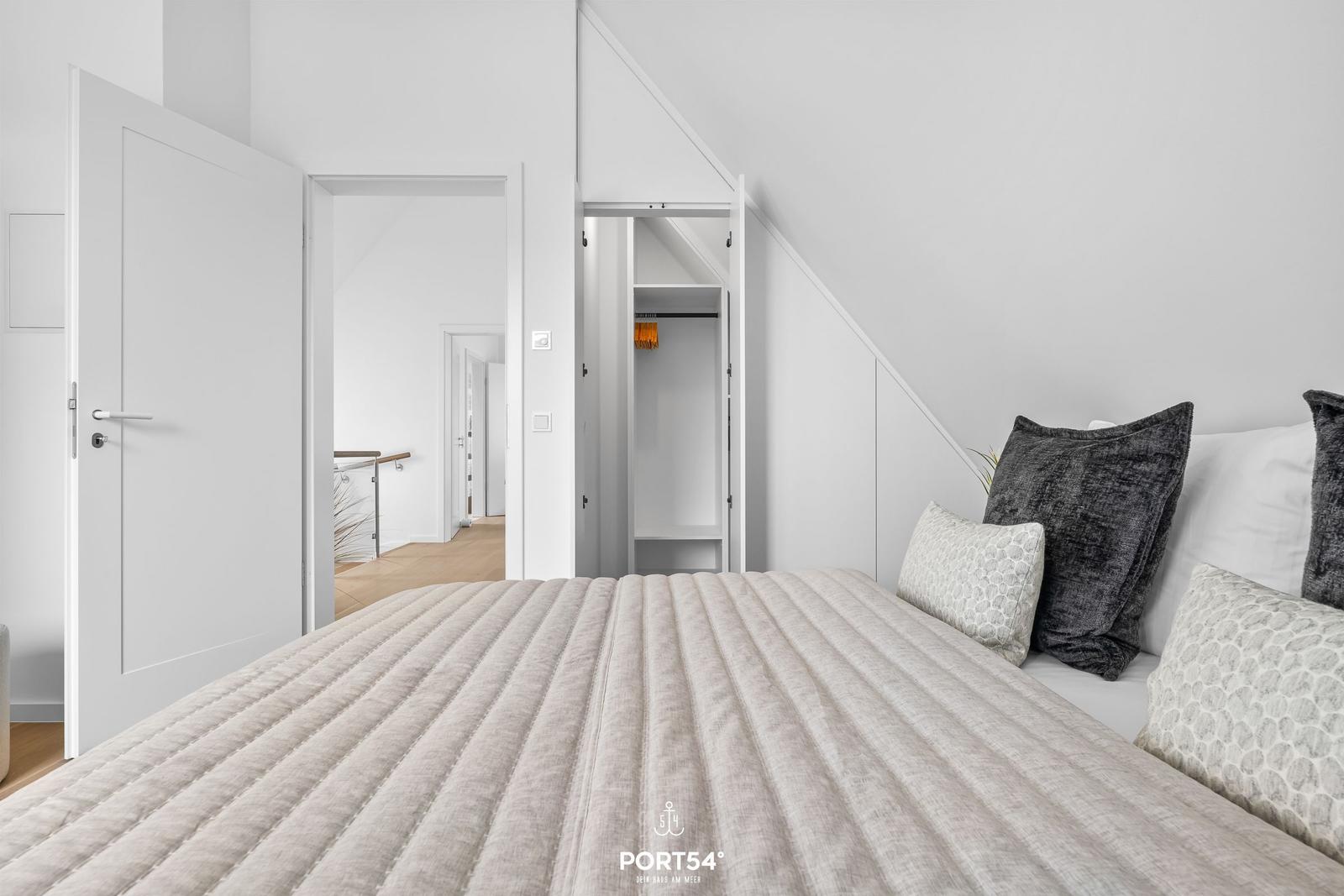 Schlafzimmer mit Dachschrägen, Bett und Kleiderschrank. Durchgänge zu weiteren Räumen.