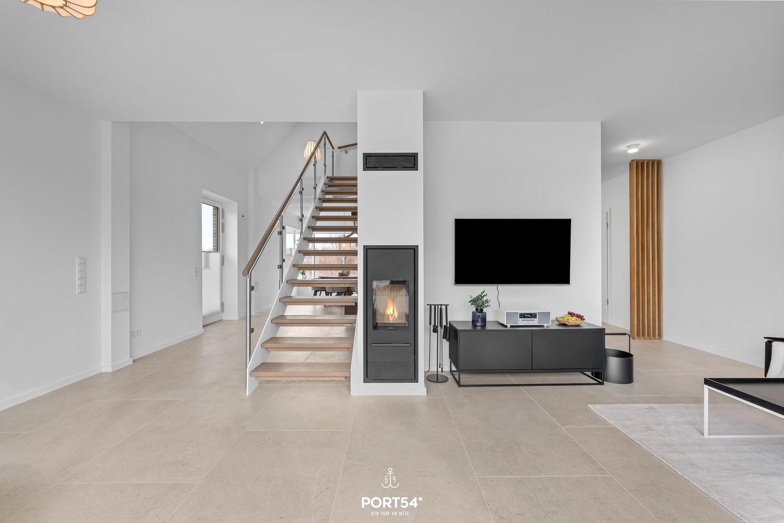 Wohnzimmer mit Kamin, Fernseher und Treppe zur oberen Etage.
