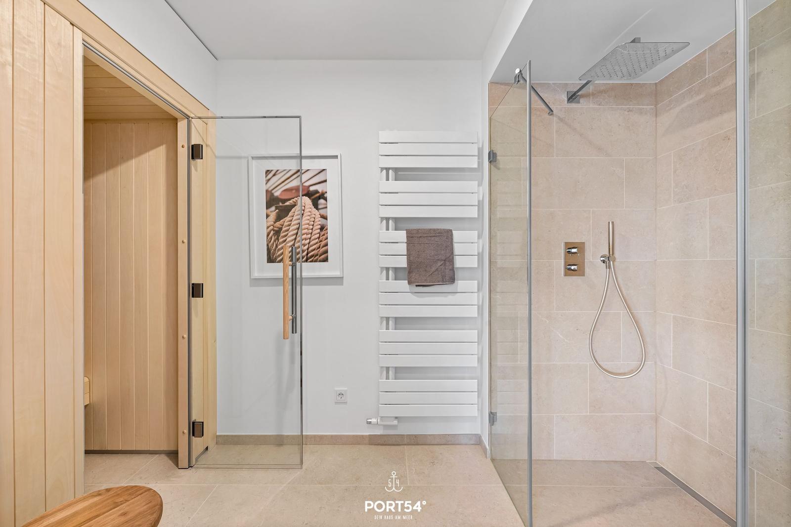 Dusche mit Regenduschkopf und Heizkörper. Sauna und Wandbild sind sichtbar.