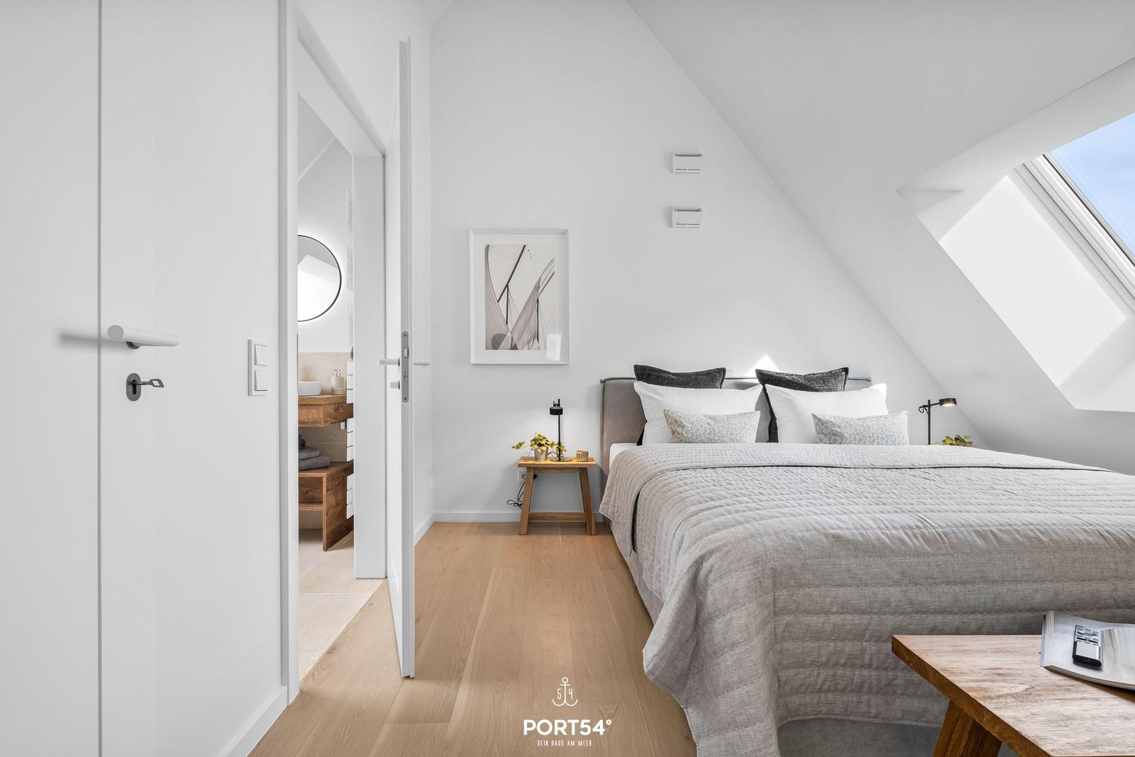 Schlafzimmer mit Dachschräge, Bett, Nachttisch und Blick auf Dachfenster.