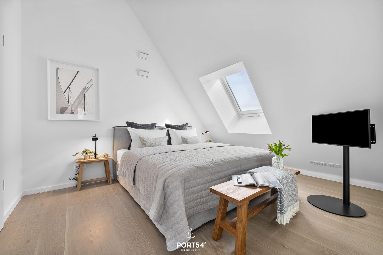 Schlafzimmer mit Dachschräge, Bett, Fenster und Fernseher.