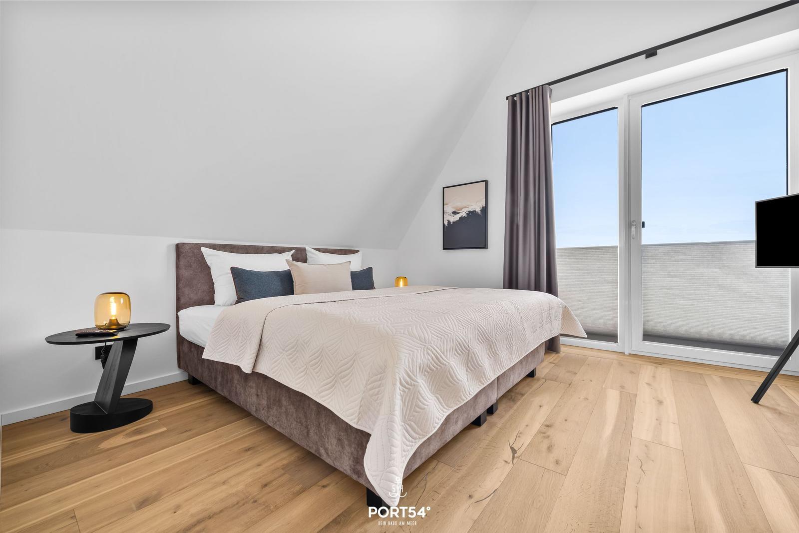 Bedroom with double bed, wooden floor, and large window with view.