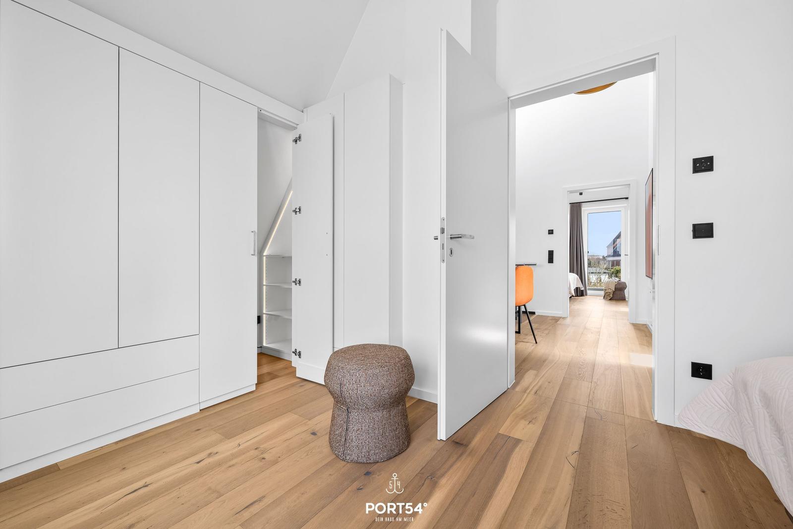 Bedroom with white closet and wooden floor. Corridor to living area with window.