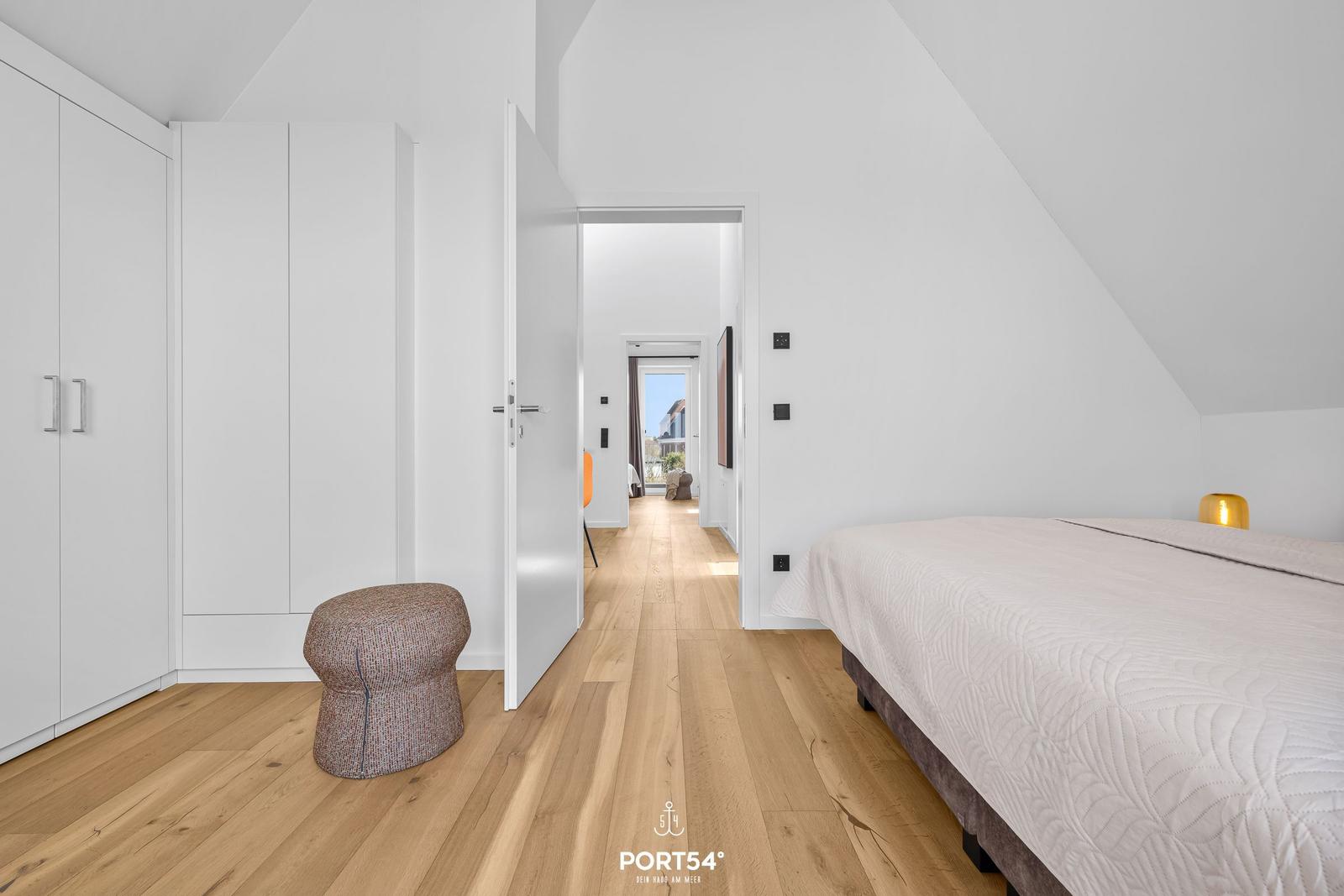 Bedroom with bed, wardrobe, and wooden floor. Corridor to living area.