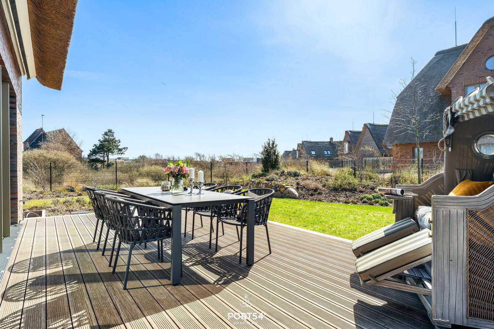 Terrace with table, chairs, and seating. Lawn and houses in the background.