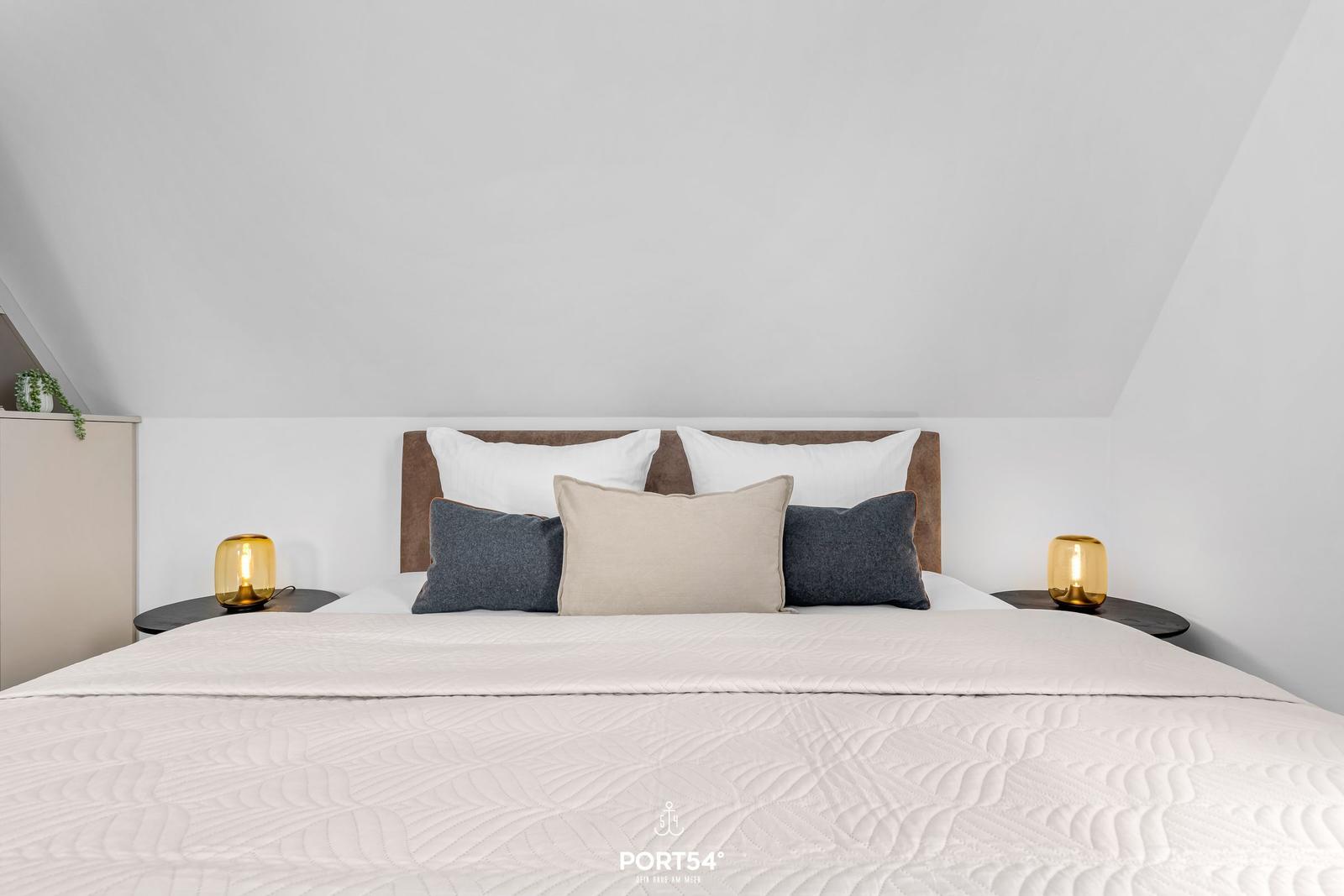 Bedroom with bed, pillows, and nightstands under sloped ceiling