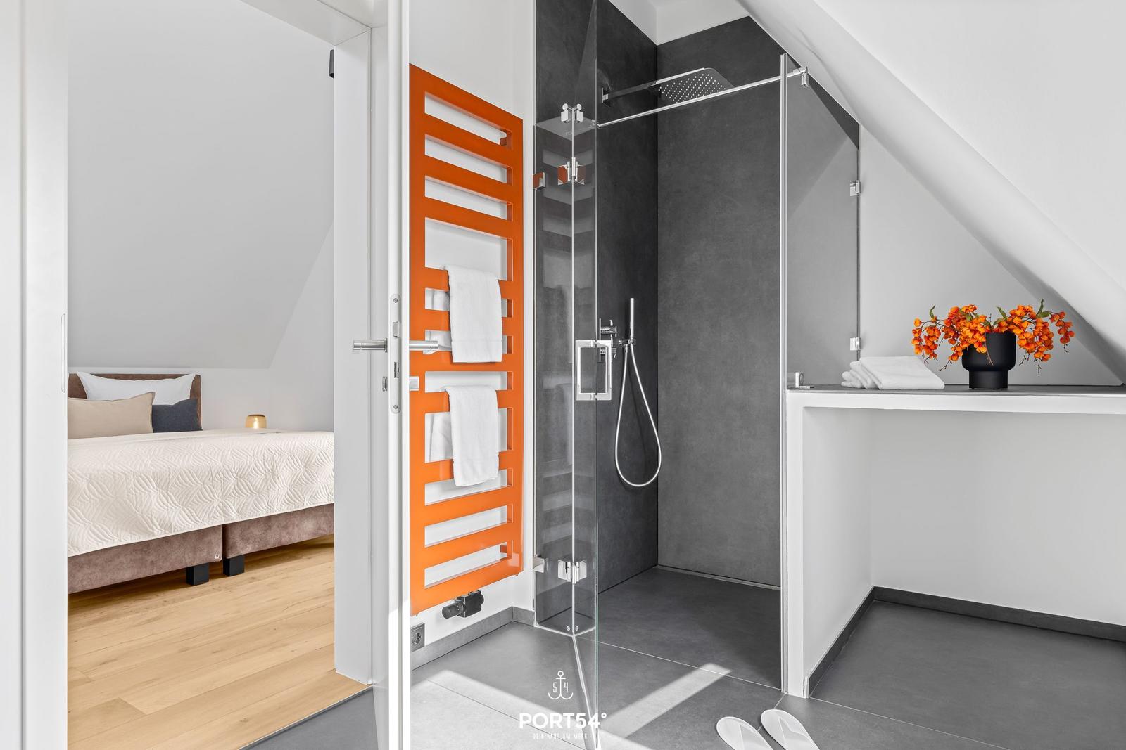 Bedroom with sloped ceiling and shower with orange towel rack.