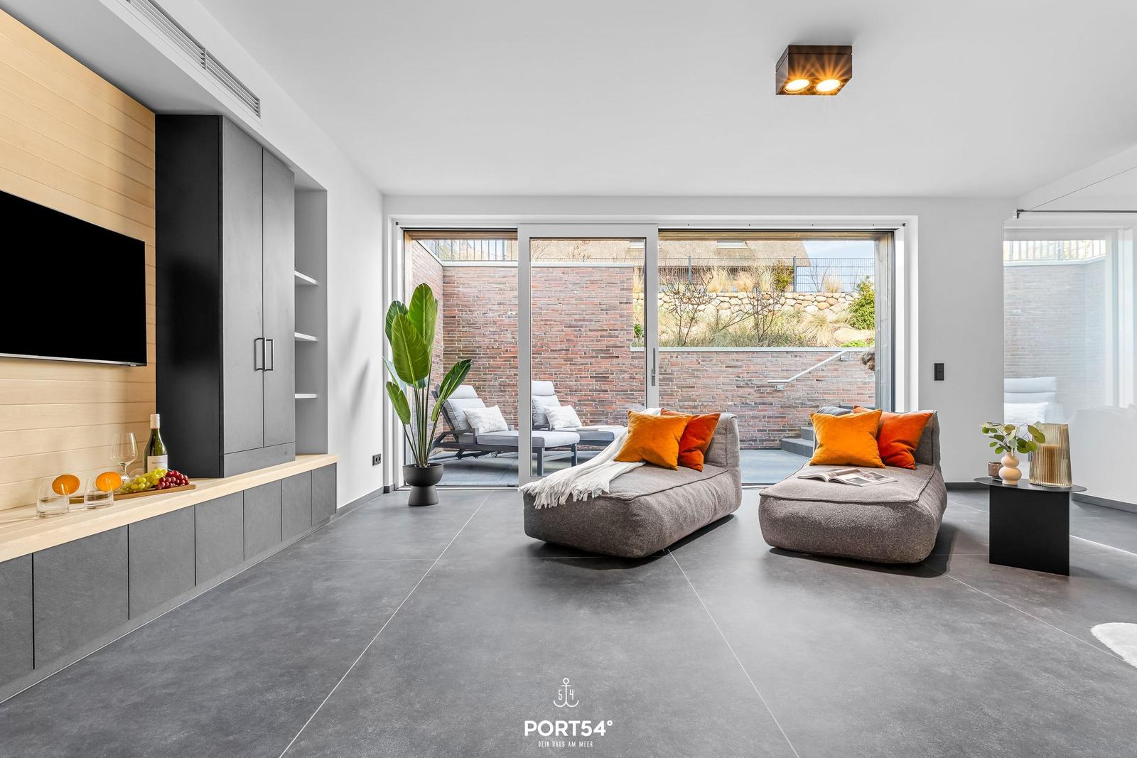 Living area with two gray chaises, orange cushions, and glass doors to terrace.