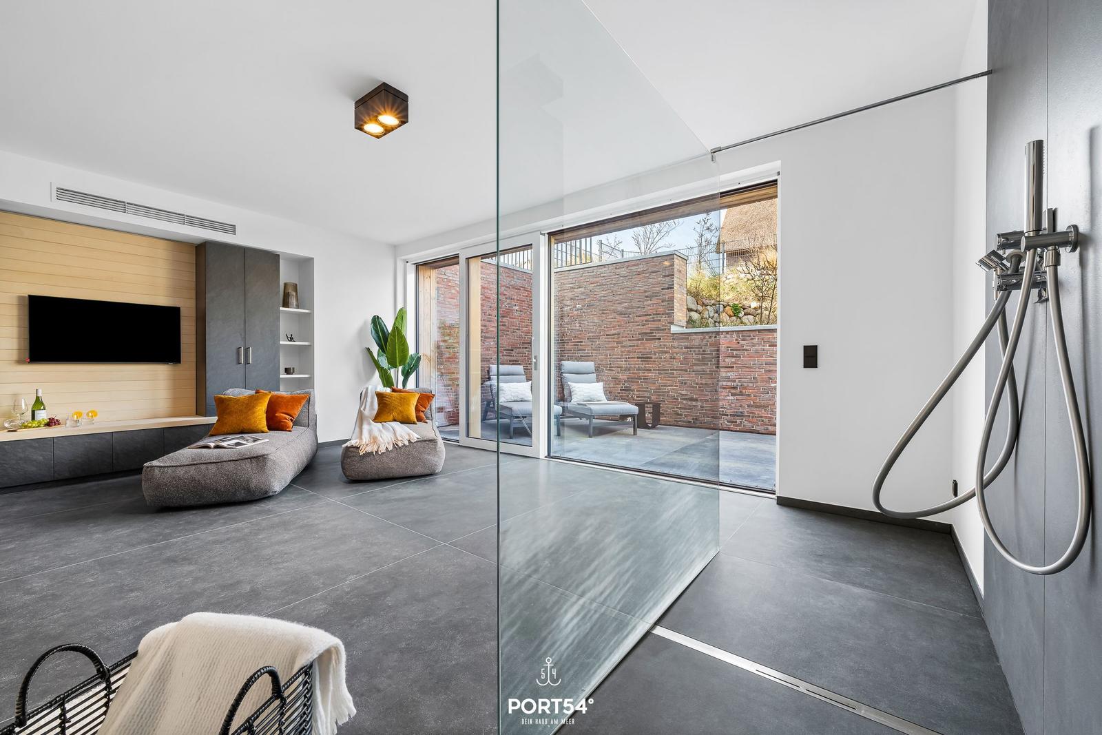 Modern living area with glass wall, loungers, and TV wall. Shower with shower head.