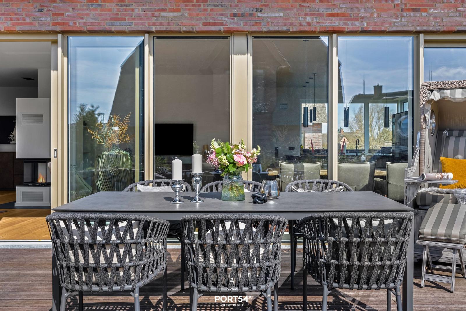 Terrace with dining table and chairs, view into the interior with fireplace.