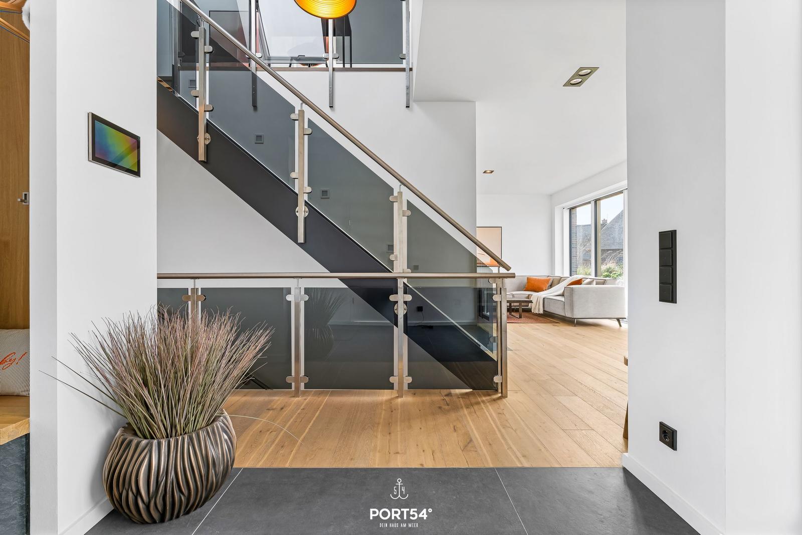 Modern staircase with glass railing leads to living area with sofa and wooden floor.