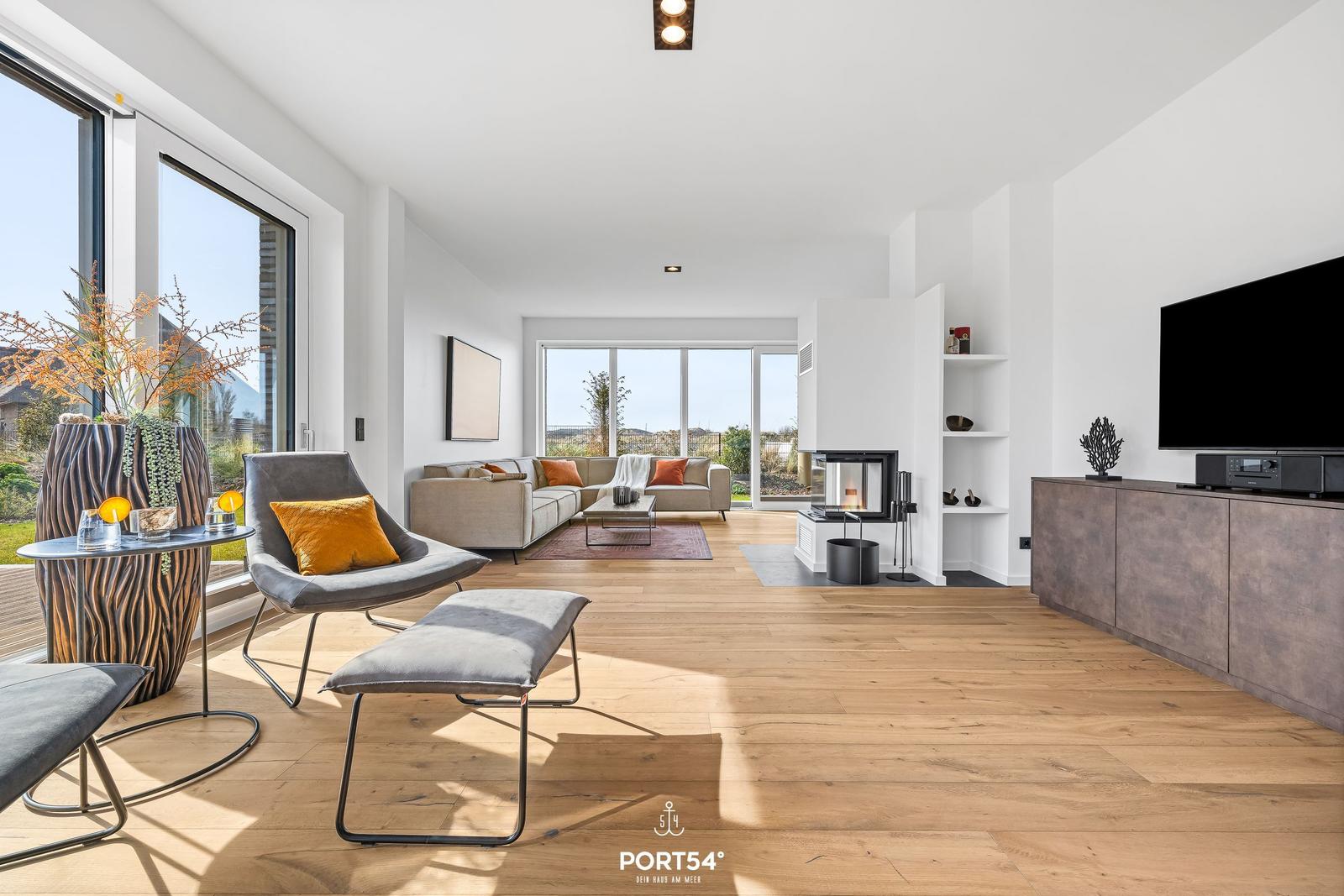 Living room with seating, fireplace and TV. Wooden floor and large windows.