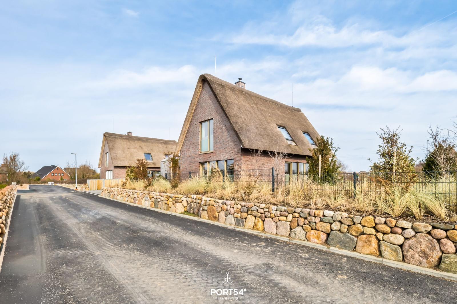 Modern villa with thatched roof and stone wall along the road.