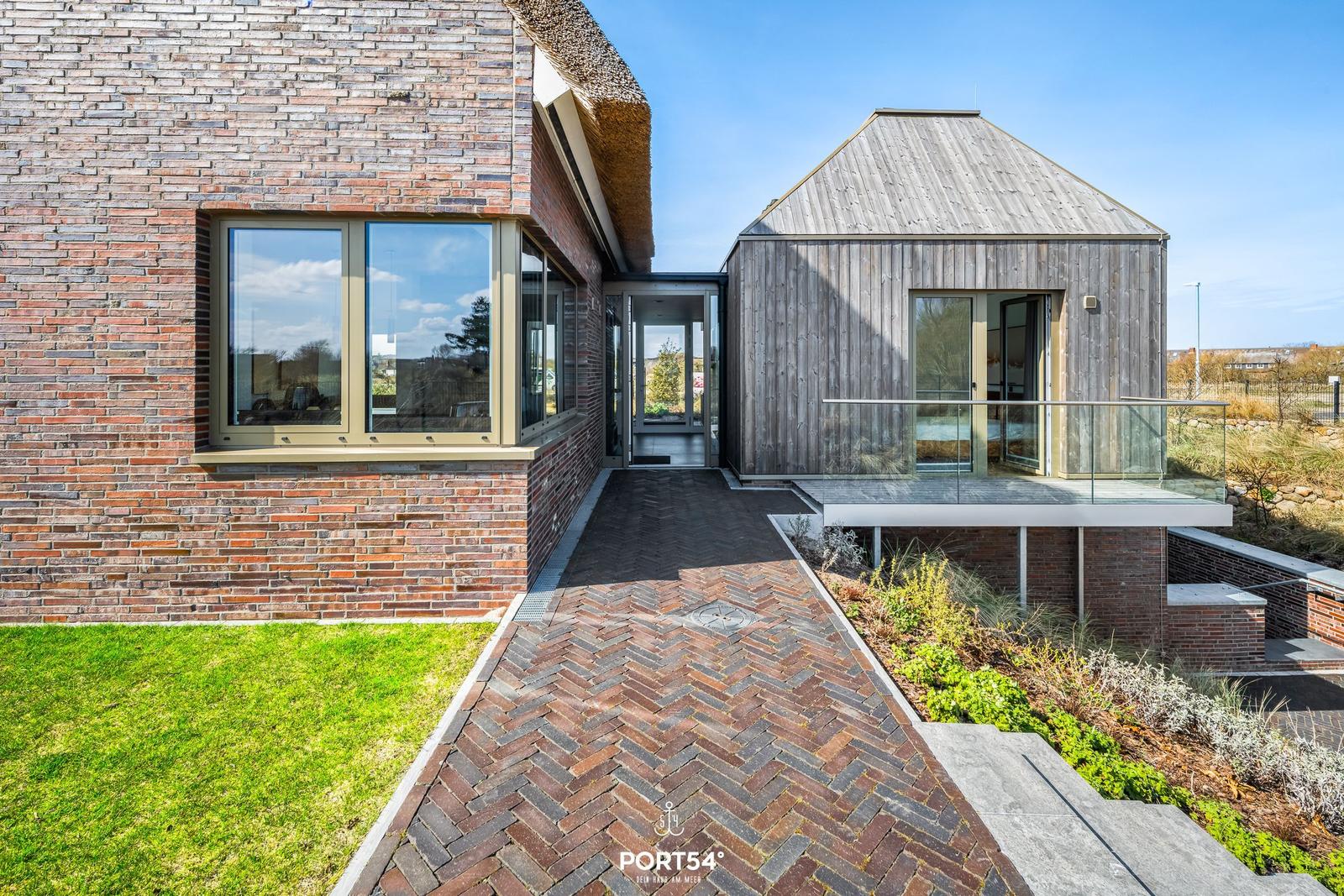 Modern villa with wooden and brick house, glass balcony, and paved path.