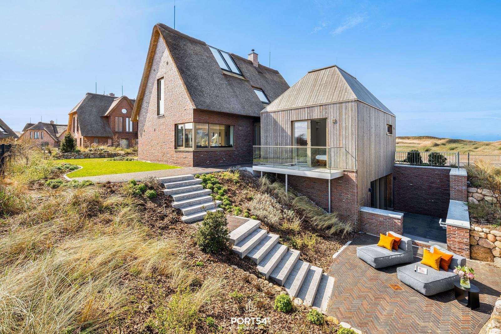 Modern villa with wooden and brick facade, terrace, and garden with dune view.