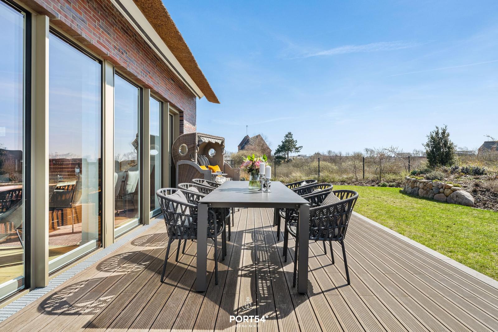 Deck with table and chairs, view of lawn and sky.