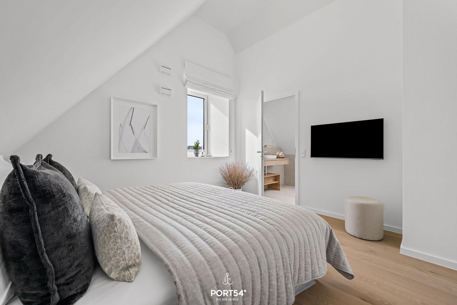 Bedroom with bed, window, and TV. Bathroom in background.