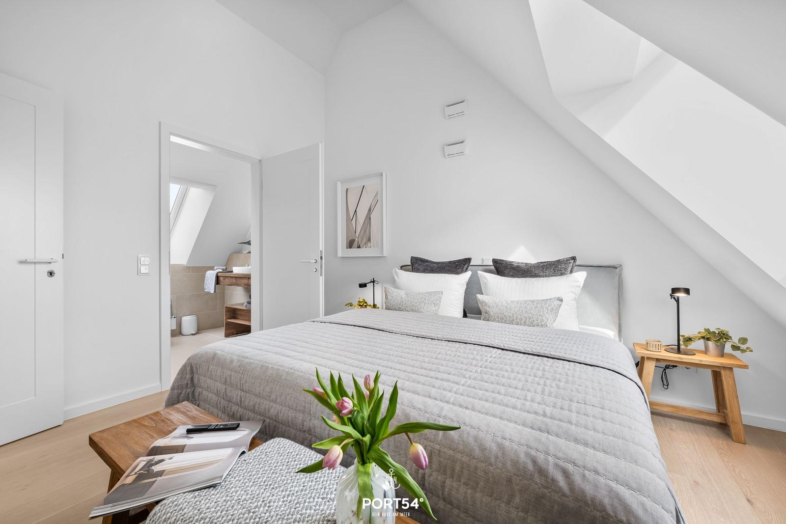 Bedroom with sloped ceiling, bed, nightstand, and view into bathroom.