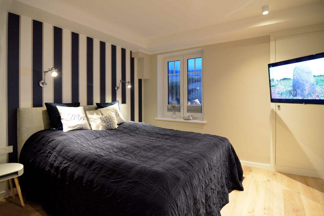 Bedroom with striped wall, bed, window, and wall-mounted TV.